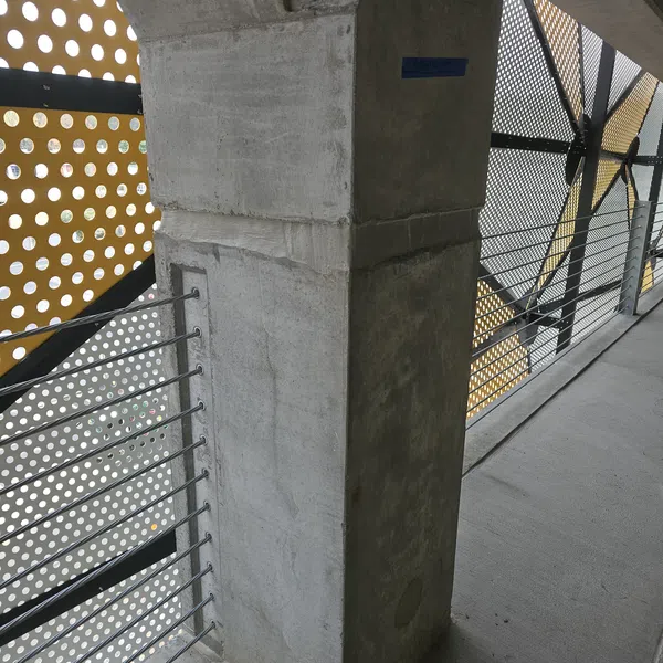 Concrete pillar and metal railing with perforated yellow and gray panels on a walkway or parking structure.
