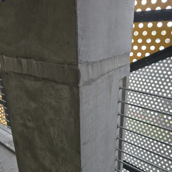 Concrete pillar with metal safety railing and perforated panel in a modern architectural setting.