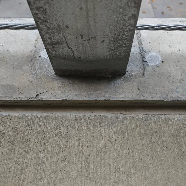 Close-up of a concrete column base connecting to a concrete slab with visible textures and metal cables.