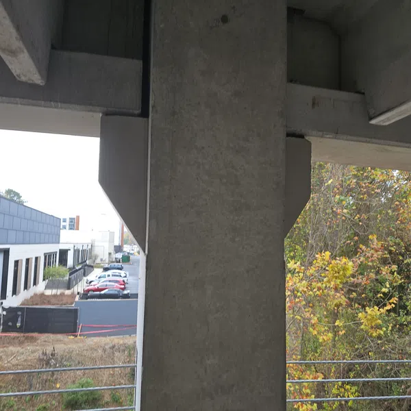 Concrete bridge pillar with railing overlooking a parking lot and autumn trees in the background.