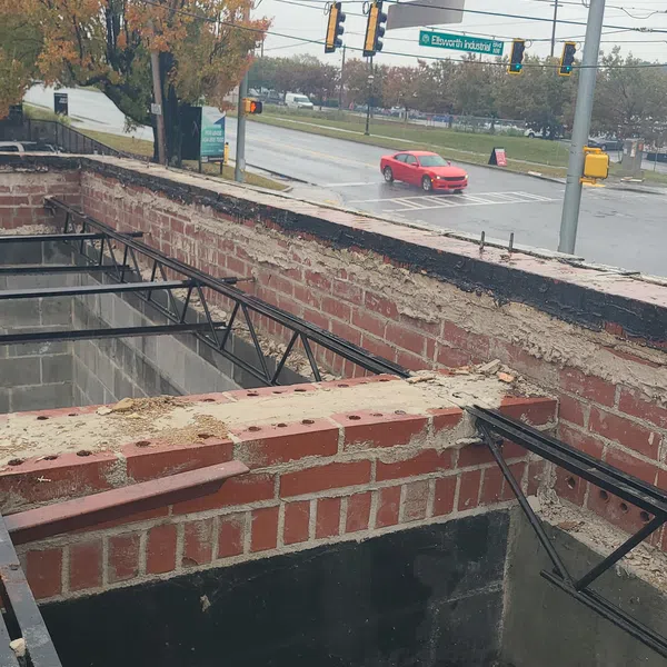 Partially demolished brick building under construction near a busy intersection with a red car and autumn trees.
