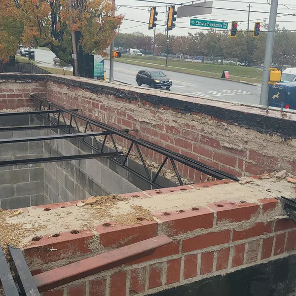 Partially built brick wall and metal framework at a construction site near a traffic light and autumn trees.