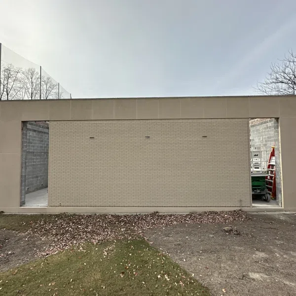 Unfinished beige brick building with two open doorways under overcast sky on a patchy grass and dirt ground.