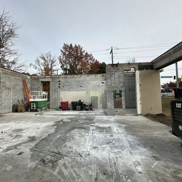 Partially constructed concrete block building with construction equipment and bare trees under a gray sky.