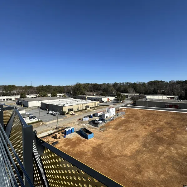 Wide view of a construction site with cleared earth, equipment, and adjacent industrial buildings under a clear blue sky