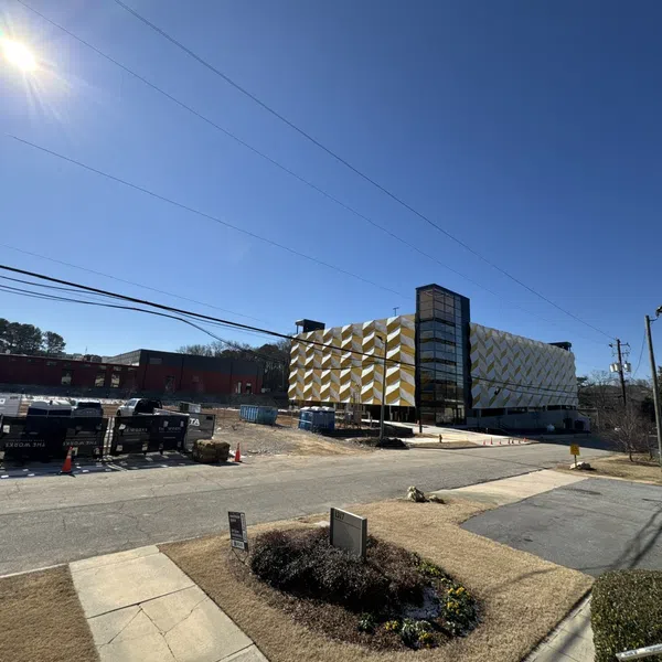 Modern multi-story building with geometric facade under clear blue sky, construction area with dumpsters nearby.