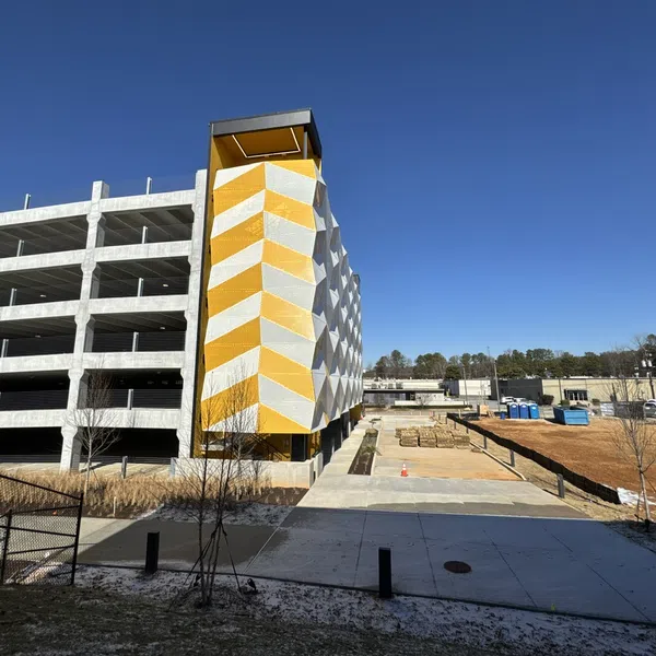 Multi-level concrete parking garage with yellow and white geometric side panel under clear blue sky.