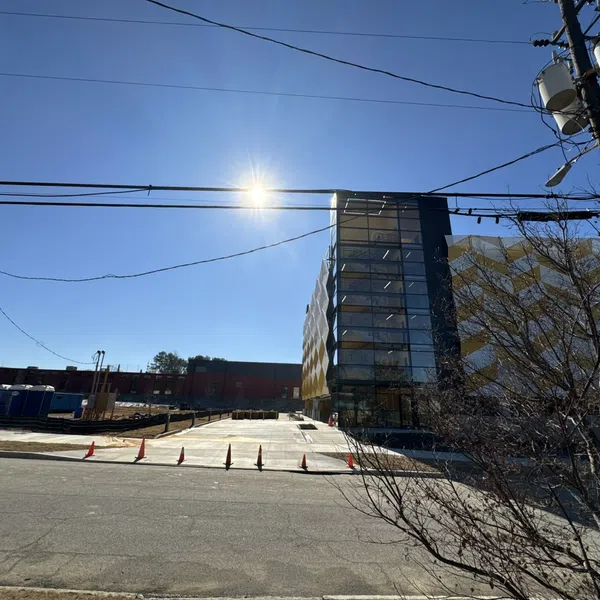 Modern building with glass facade and geometric pattern under clear blue sky with sun and power lines.