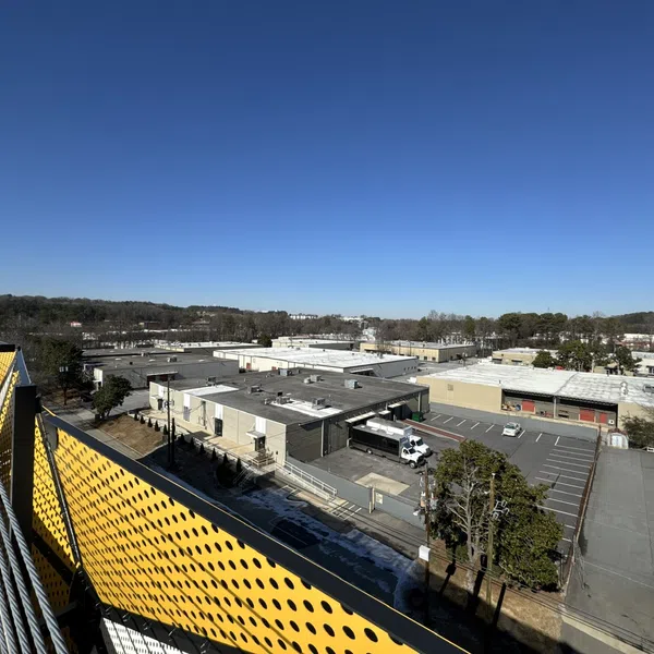 View over industrial warehouse rooftops and parking lots under a clear blue sky with a yellow perforated railing in the foreground.