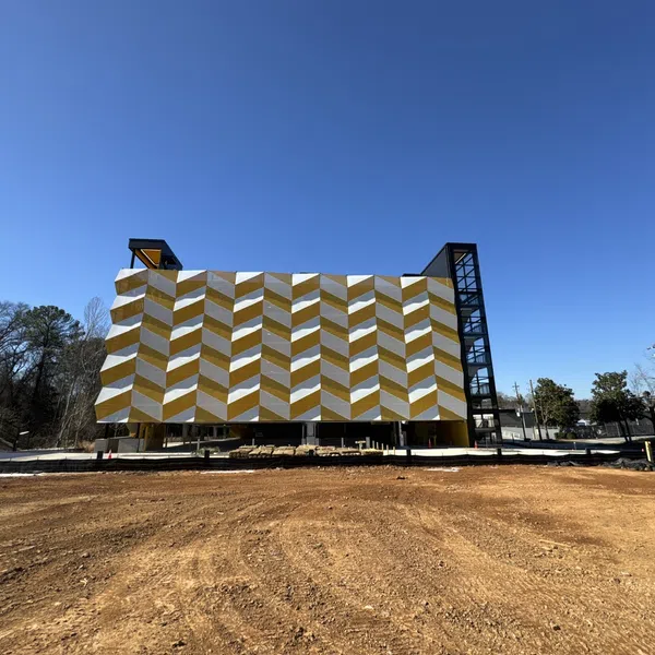 Modern building with bold yellow and white geometric facade against clear blue sky on dirt lot.