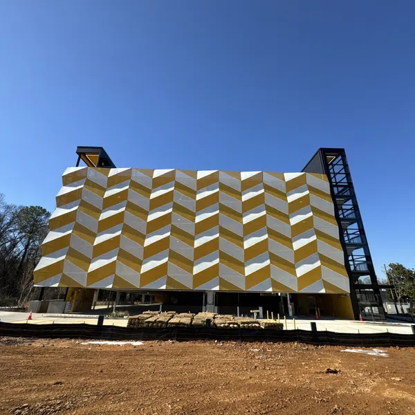 Modern building with gold and white chevron pattern facade under clear blue sky and surrounding trees.