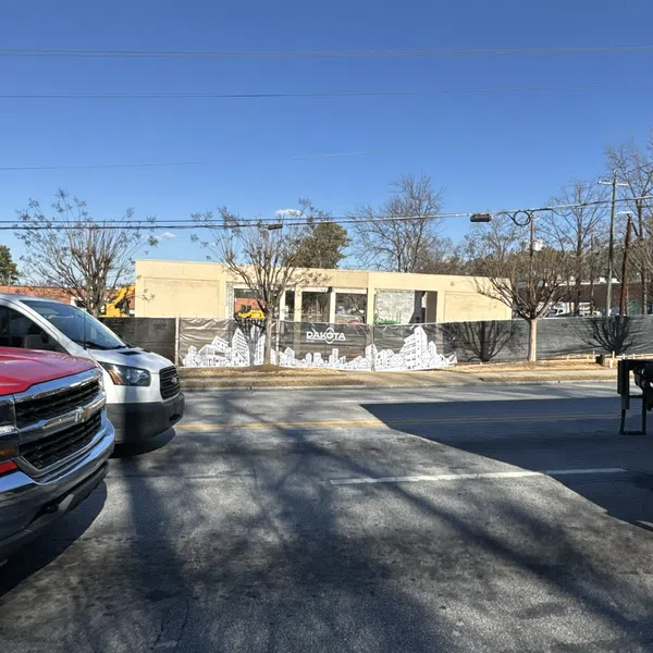 Daytime street view with parked trucks and a construction site with Dakota signage and white cityscape artwork panels.