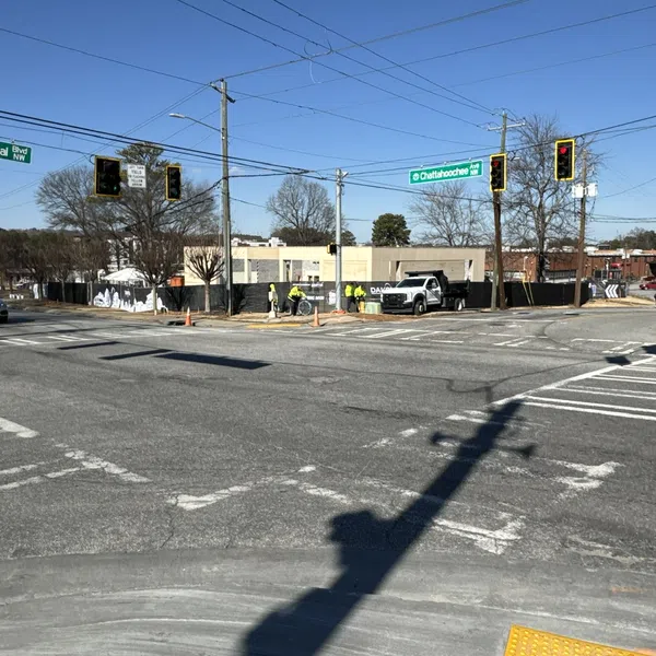Traffic intersection with stoplights, street signs for Ellsworth Industrial Blvd NW and Chattahoochee Ave, and workers in safety vests.