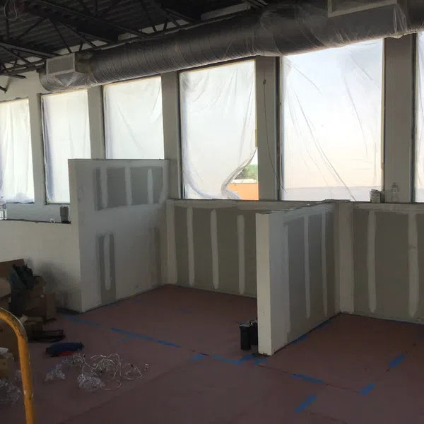 Office space under construction with drywall partitions and large windows covered in plastic sheeting.