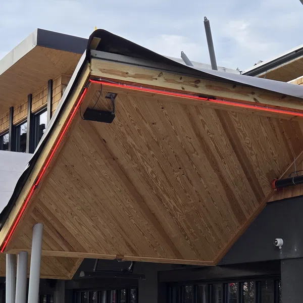 Modern building with angled wooden awnings and red LED strip lighting under a cloudy sky