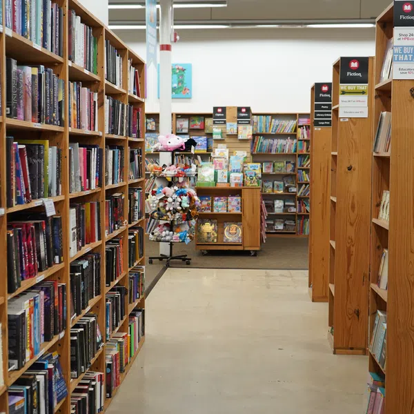 Interior view of a bookstore aisle with wooden shelves filled with books and a display stand with plush toys.