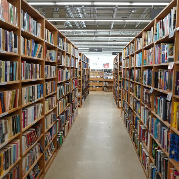 Aisle view of a well-lit library with tall wooden bookshelves filled with diverse books on both sides.
