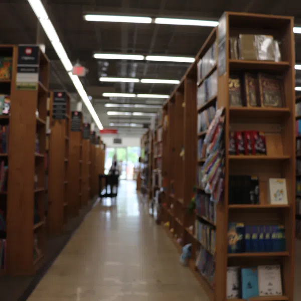 Aisle view of wooden bookshelves filled with books inside a well-lit bookstore or library.