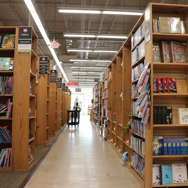 Wide aisle between tall wooden bookshelves filled with books in a bright bookstore or library.