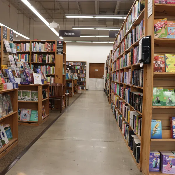 Wide aisle between tall wooden bookshelves filled with books in a well-lit bookstore or library section.