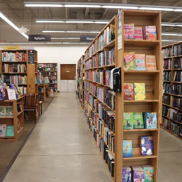 Interior of a well-lit bookstore with multiple wooden shelves filled with books and clear aisle signs.