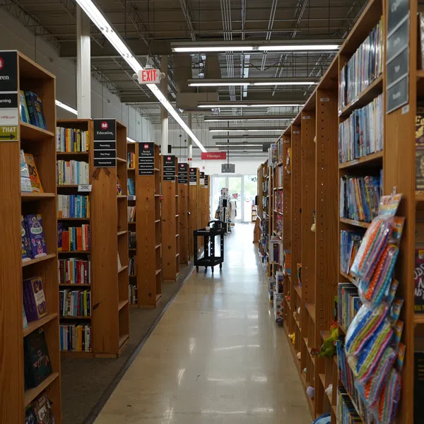 Long aisle between tall wooden bookshelves filled with books in a well-lit bookstore or library.