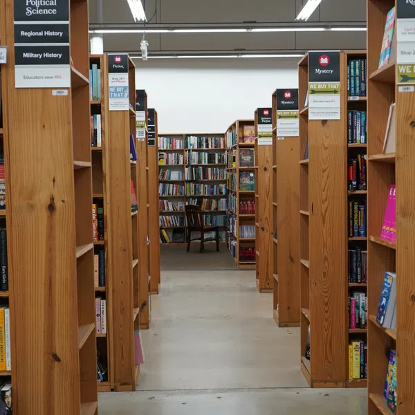 Aisle in bookstore with wooden shelves filled with books, signs for Political Science and Mystery sections overhead.