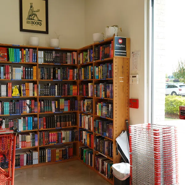 Corner bookshelf filled with colorful books inside a store with red shopping baskets and natural light.