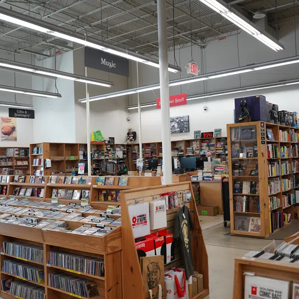 Interior of a bookstore with wooden shelves filled with books, music CDs, and merchandise under bright lighting.