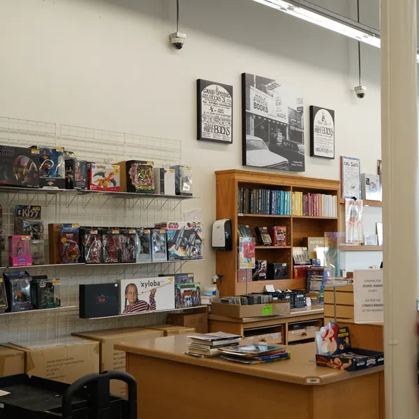 Interior of a bookstore featuring shelves with books, collectibles, and a wooden counter with stacked books.