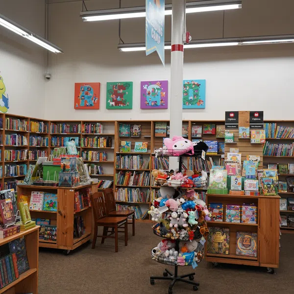 Children's section of a bookstore with colorful bookshelves, plush toys on a rotating rack, and reading area.