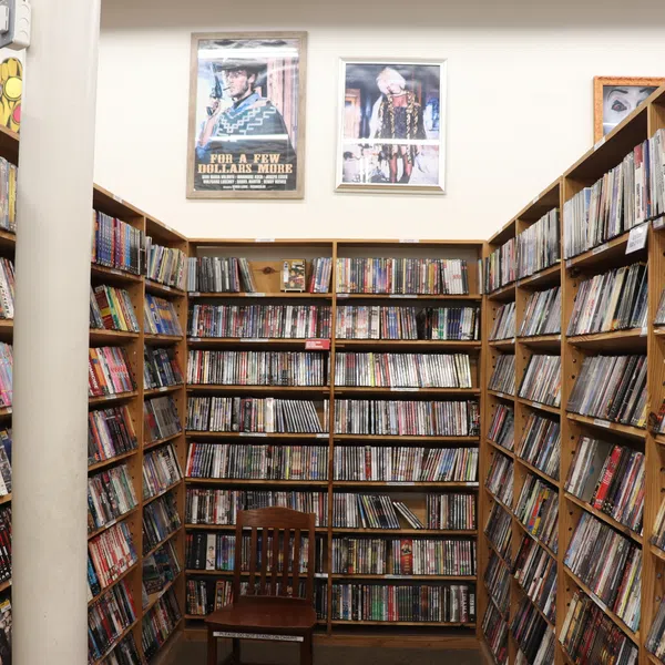 Wooden shelves packed with DVDs and movies surround a wooden chair in a well-lit small media library room.