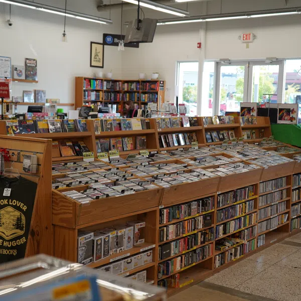 Interior of a well-lit bookstore with wooden shelves filled with books and merchandise like library tote bags and shirts.