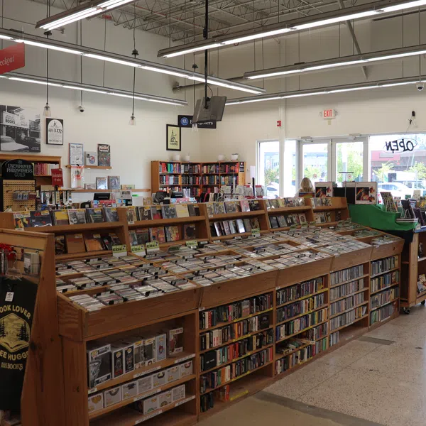 Interior of a bookstore with wooden shelves filled with books and DVDs under bright ceiling lights.