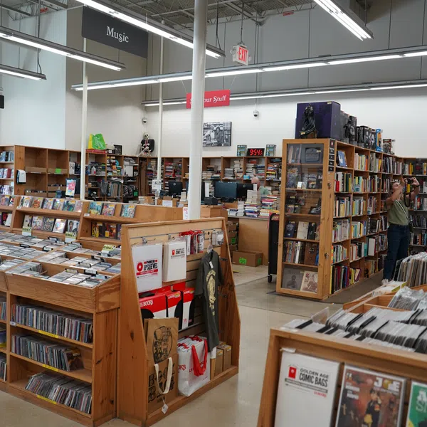 Interior of a bookstore with wooden shelves filled with books, comics, CDs, and a person taking photos inside.