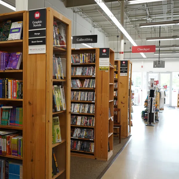 Interior of a store with wooden shelves labeled Graphic Novels, Collectibles, DVDs, and a visible checkout sign.