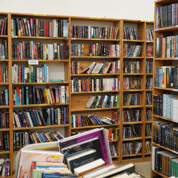 Interior of a bookstore with wooden shelves filled with diverse books and a front table stacked with notebooks and books