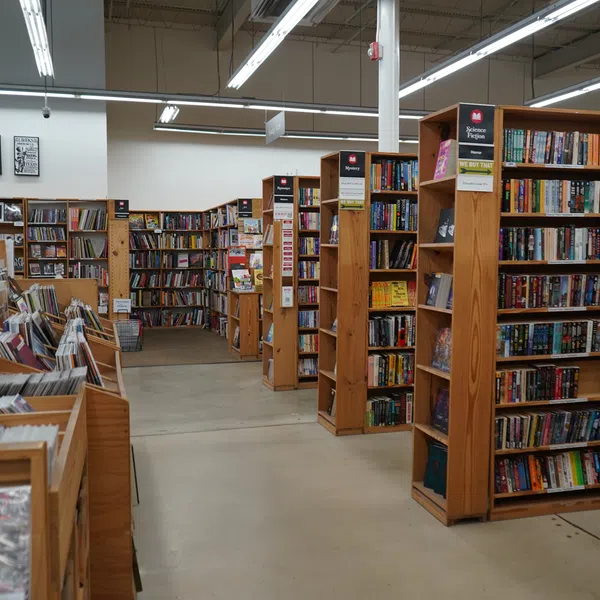 Interior of a bookstore with wooden shelves filled with books and magazines under bright fluorescent lights.