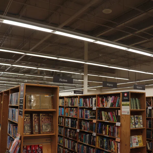 Interior view of bookstore with shelves labeled Fiction, History, Religion filled with books under bright lighting.