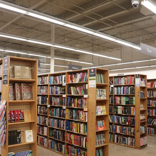 Interior of a brightly lit bookstore with wooden shelves full of books organized by genre and category signs.