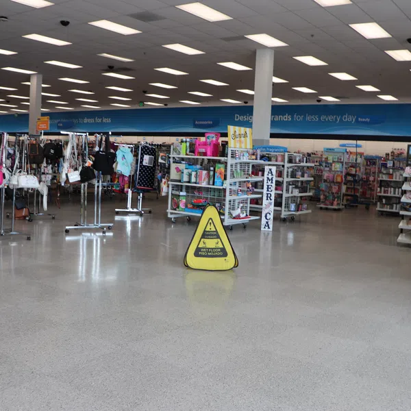 Interior of retail store with clothing racks, accessories, and a caution wet floor sign on polished floor.
