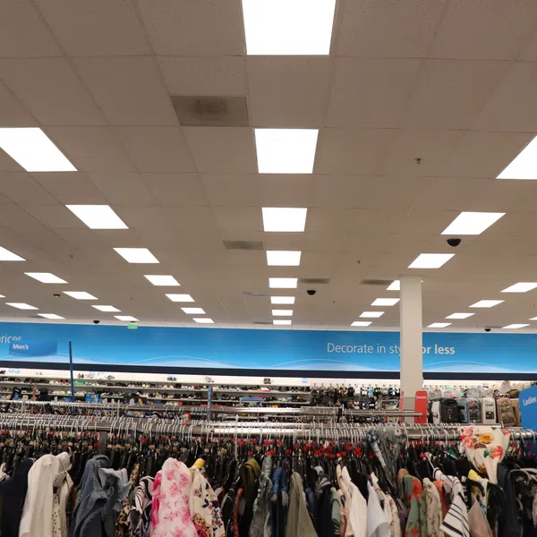 Clothing racks filled with various apparel inside a well-lit department store with a blue banner overhead.