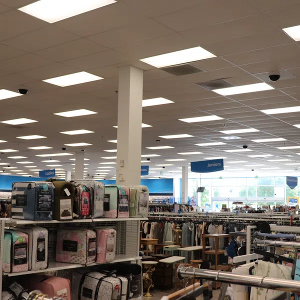 Interior view of a well-lit retail store with shelves of bedding and racks of clothing labeled Juniors and Ladies.