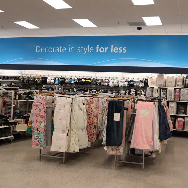 Retail store aisle with bedding, linens, and home decor items under a sign reading Decorate in style for less