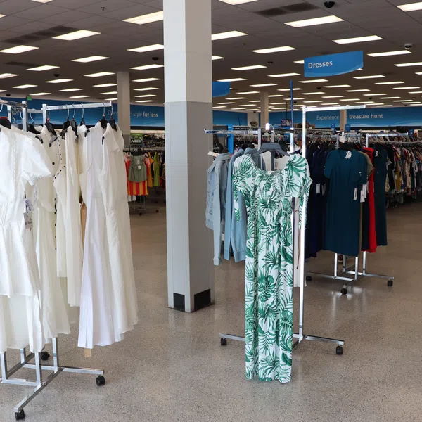 Clothing racks in a bright retail store displaying white dresses and tropical patterned dresses under blue category signs.