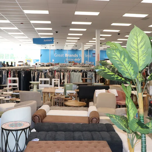 Furniture, decor, and clothing racks arranged in a bright department store interior under fluorescent lights.