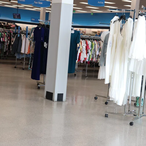 Interior of a clothing store with racks of white dresses and assorted apparel and a woman with a walker.