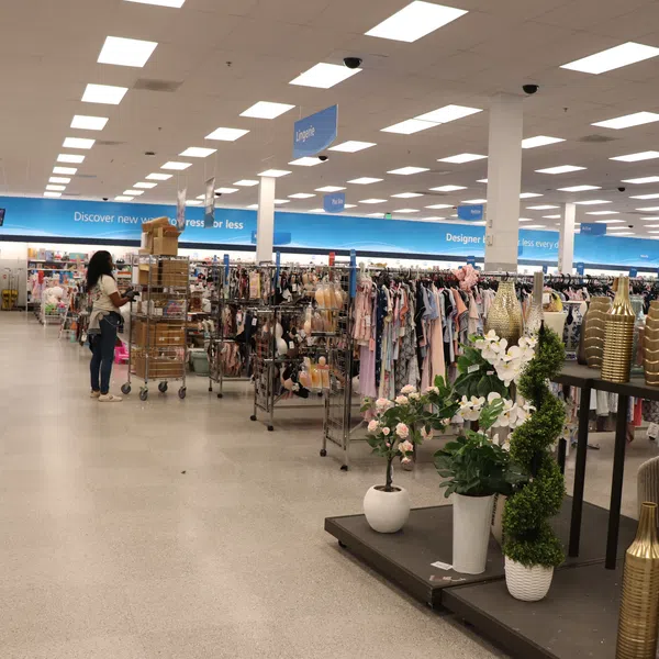 Inside a large store with aisles of clothing racks, home decor, and a shopper pushing a cart.