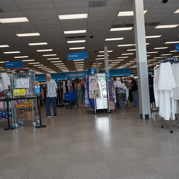 Wide view of a retail clothing store interior with racks of dresses, juniors, and ladies sections and shoppers browsing.