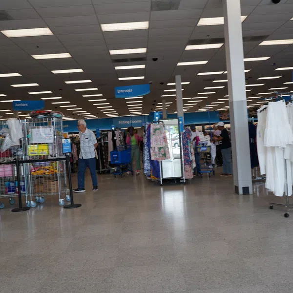 Interior view of a clothing store with sections for juniors, dresses, and ladies featuring racks of white and colorful garments.